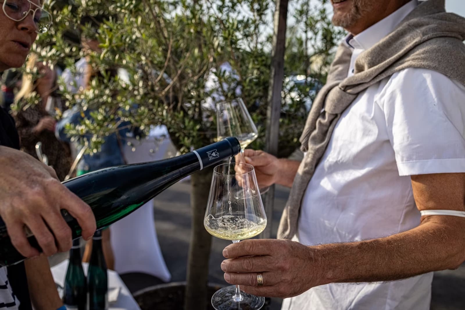 Ein Gastgeber schenkt im Freien Weißwein in das Glas eines Gastes ein